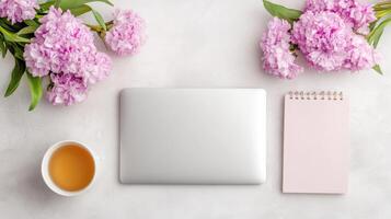 Top view of a laptop, notebook, cup of tea and flowers on a white background photo