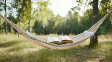 Cozy hammock strung between trees holds open book, inviting relaxation in nature photo