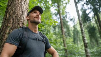 Hiker pausing beside tree, enjoying nature and reflecting in forest photo