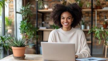 Smiling woman with curly hair working on laptop in cozy workspace surrounded by plants photo