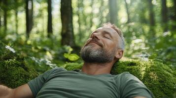 A man with a beard and green shirt is lying on a moss covered forest floor photo