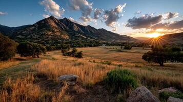 The sun sets over a mountain range and grassy field photo