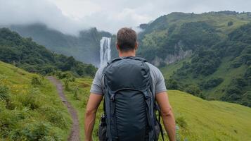 A man with a backpack standing on a trail with a waterfall in the background photo
