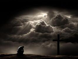 Man kneeling in prayer near a cross under dark clouds photo