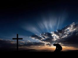 Silhouette of a person praying beside a cross at sunset photo
