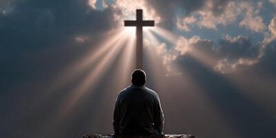Person reflecting under a cross with radiant light in the sky photo
