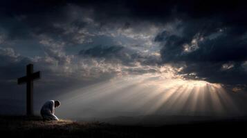 A man kneels at the cross and looks at the sun rays photo