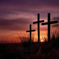 Three crosses are silhouetted against a sunset photo