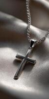 Silver cross pendant resting on satin fabric photo