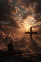 Man sits in contemplation under a cross in the clouds photo