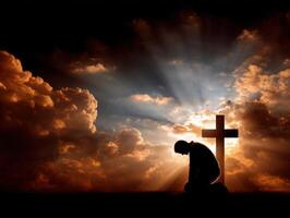 Man kneeling in prayer before a cross at sunset photo
