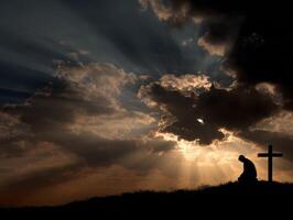 Silhouette of a person kneeling before a cross at sunset photo