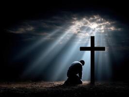Man kneeling near cross under beams of light at dusk photo