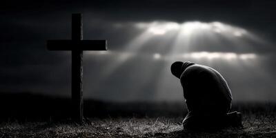 A man kneels down in front of a cross photo