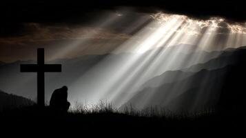 Man kneeling beside cross in serene mountain landscape photo