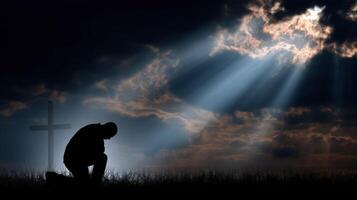 Person kneeling in prayer under rays of light at dusk photo