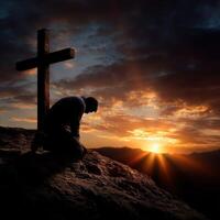 Man praying at a cross during a beautiful sunset photo