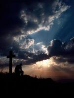 silueta de un persona Orando cerca un cruzar a puesta de sol foto