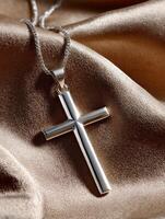 Elegant silver cross pendant resting on soft satin fabric photo
