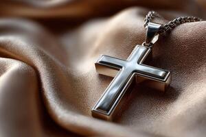 Silver cross pendant resting on golden silk fabric photo