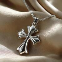 Silver cross pendant resting on smooth satin fabric photo