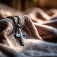 Silver cross necklace resting on soft fabric in natural light photo