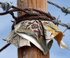 Fabric scraps tied to a wooden pole alongside barbed wire photo