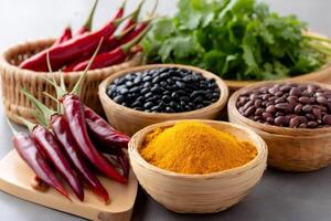 Turmeric, beans, chili peppers and coriander are displayed in small wicker bowls on a gray tabletop photo