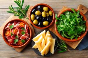 Spanish tapas with jamon, manchego cheese, olives and arugula salad on wooden table photo