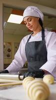 Woman in chef uniform uses a rolling pin on dough while preparing croissants at a clean bakery workstation near a window video