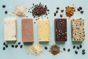 Five different types of handmade soap are arranged neatly on a light blue surface, complemented by various natural ingredients like coffee and spices photo