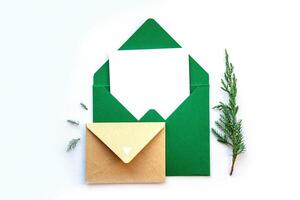 Elegant green envelopes with a blank card and a pine sprig on a white background for a seasonal greeting photo