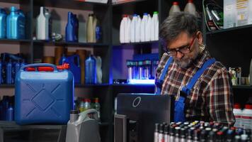 Mature male clerk in plaid shirt and overalls scans motor oil container with barcode reader while performing inventory in an automotive store video