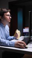 vertical Office worker eating banana while working on computer at night video