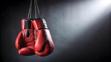 Red boxing gloves hanging in a dark training space under bright light photo