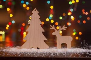 Wooden toy deer and spruce on a dark table with white snow. photo