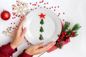 New Year's table decor. Female hands hold a plate with a cucumber snack in the form of a Christmas tree photo
