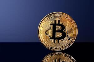 Shiny bitcoin coin on reflective surface with dark blue background photo
