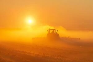 Tractor harvesting at sunset in a dusty field photo