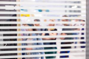 Blurred figures of people seen through the slats of window photo