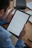 A white man, 30 years old, holding a tablet with a blank screen, on a wooden desk with a tablet photo