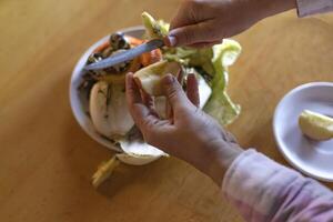 hands peeling an apple with a knife over a food waste container photo