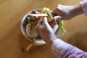 hands peeling an apple over a food waste container photo