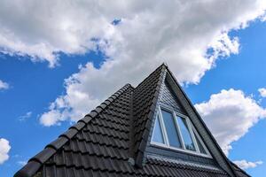 Dark tiled roof with dormer window under blue sky with white clouds photo