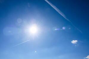 Bright sun shining in a deep blue sky with contrails photo
