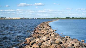 Stone pier stretching across a calm body of water under a bright blue sky with scattered clouds photo