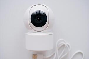 Close-up image of a modern white smart security camera mounted on a wall with a USB cable attached photo