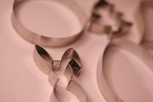 Close-up view of stainless steel cookie cutters in festive shapes, including a bunny and a Christmas tree, placed on a soft pink background photo