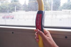 Hand presses stop button on bus while commuting in city photo