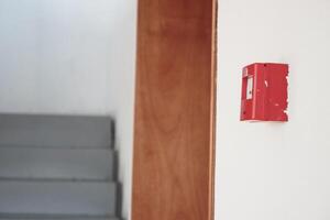 Fire alarm mounted on wall near staircase in indoor building setting photo